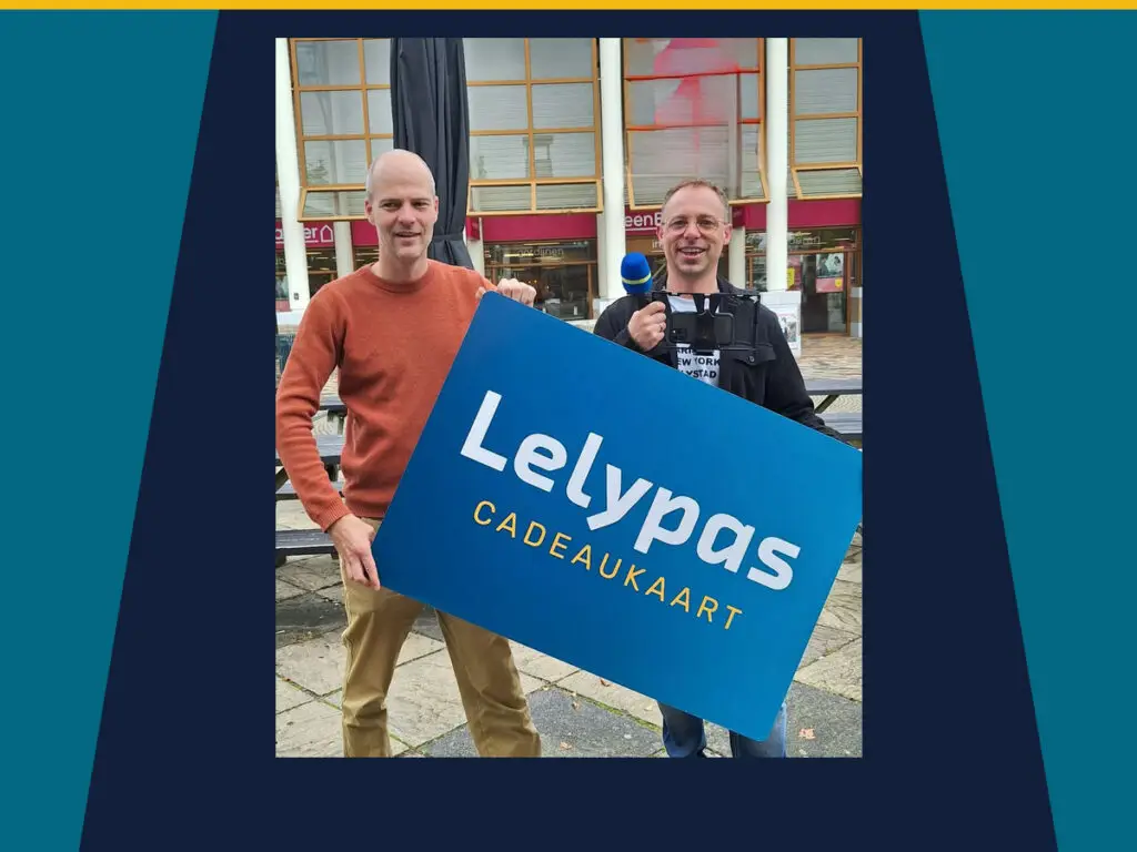 Twee mannen tijdens een Lelypas-videodraaidag in Lelystad, met een groot bord van de Lelypas Cadeaukaart.