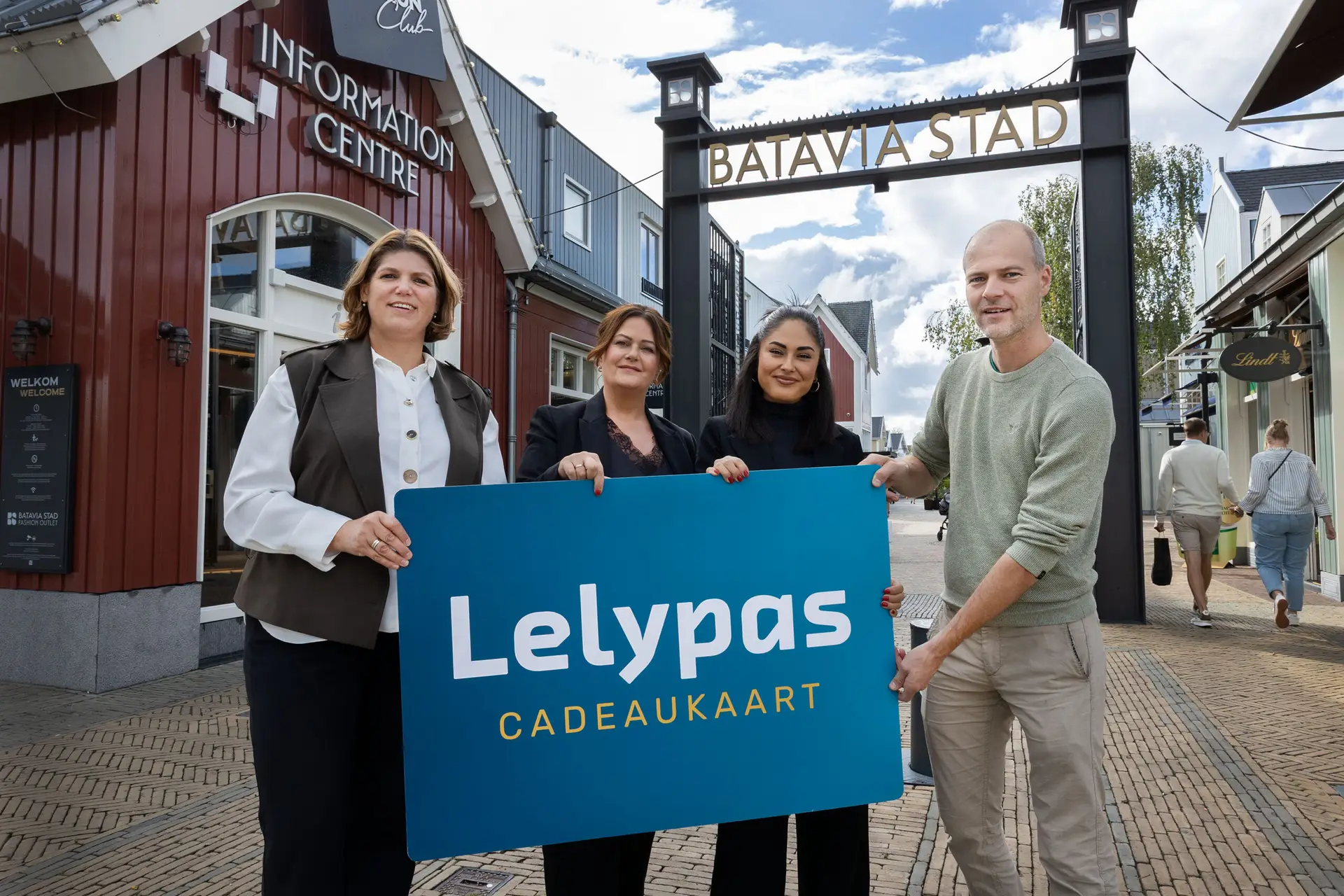 Liselore, Barbara en Meltem van Batavia Stad Information Centre en Yorick Lindeman van Stichting Lelypas met een Lelypas-bord bij de ingang van Batavia Stad.