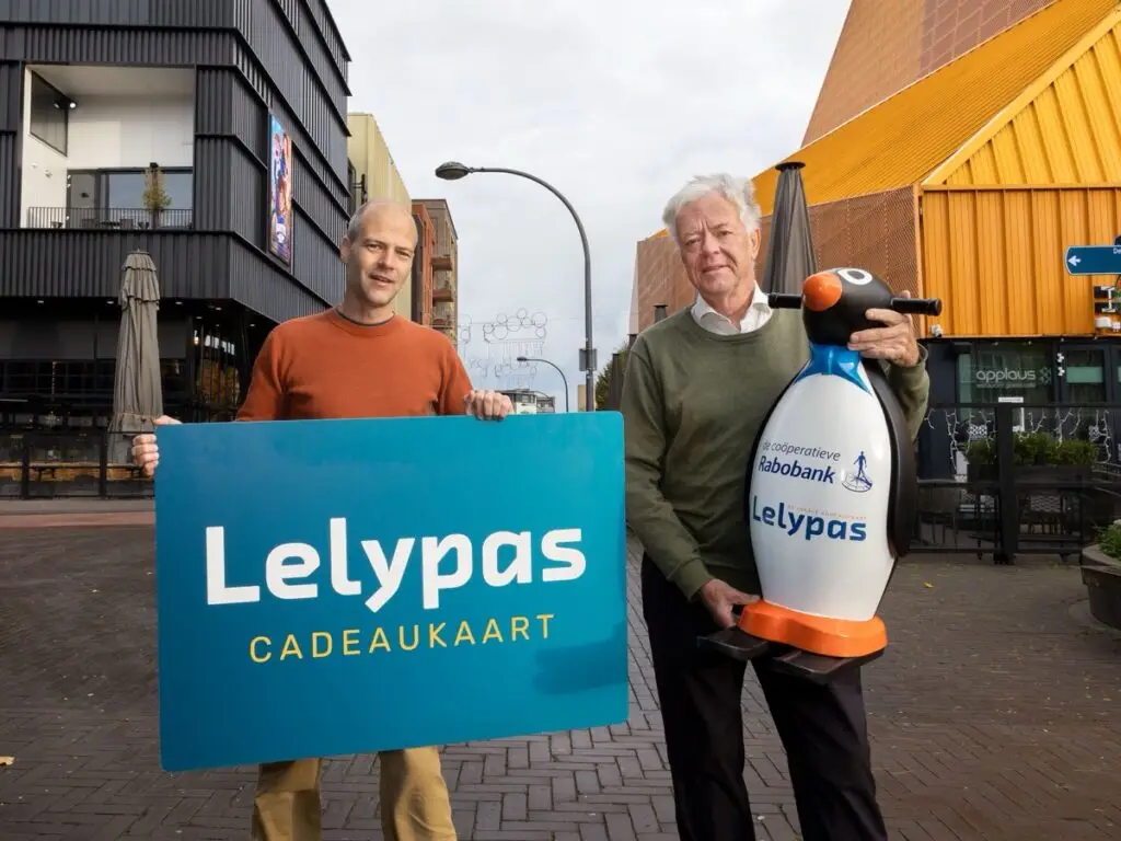 Yorick Lindeman van Stichting Lelypas en een vertegenwoordiger van Lelystad On Ice met een Lelypas-bord en de schaatspinguïn op het Agorahof.